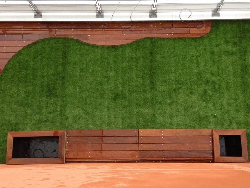 Aménagement extérieur avec platelage en bois exotique courbé et pelouse synthétique verte. Banc et deux jardinières intégrées.