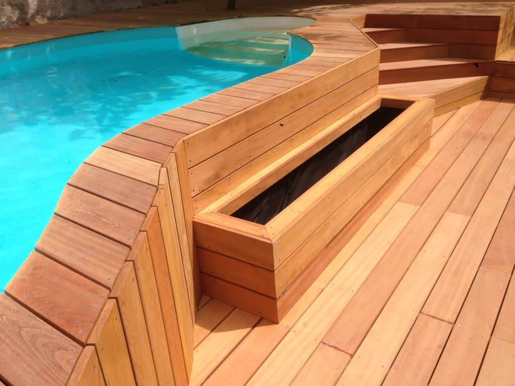 Aménagement piscine : Terrasse bois exotique avec jardinière. Aménagement de piscine avec terrasse en bois courbe, marches d'accès et jardinière intégrée. Eau turquoise éclatante.