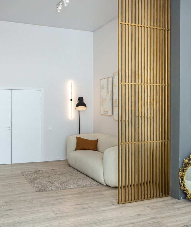 Claustra doré et canapé bouclé : design moderne. Canapé bouclé beige dans un salon moderne avec sol en bois clair. Un claustra doré à lattes sépare l'espace près d'une double porte.