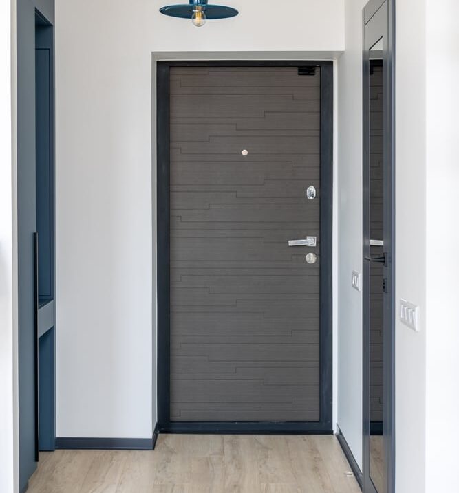 Porte d'entrée design gris foncé et couloir moderne lumineux Couloir d'entrée moderne avec murs blancs, plancher bois clair. Porte d'entrée gris anthracite texturée encadrée de noir. Suspension bleue.